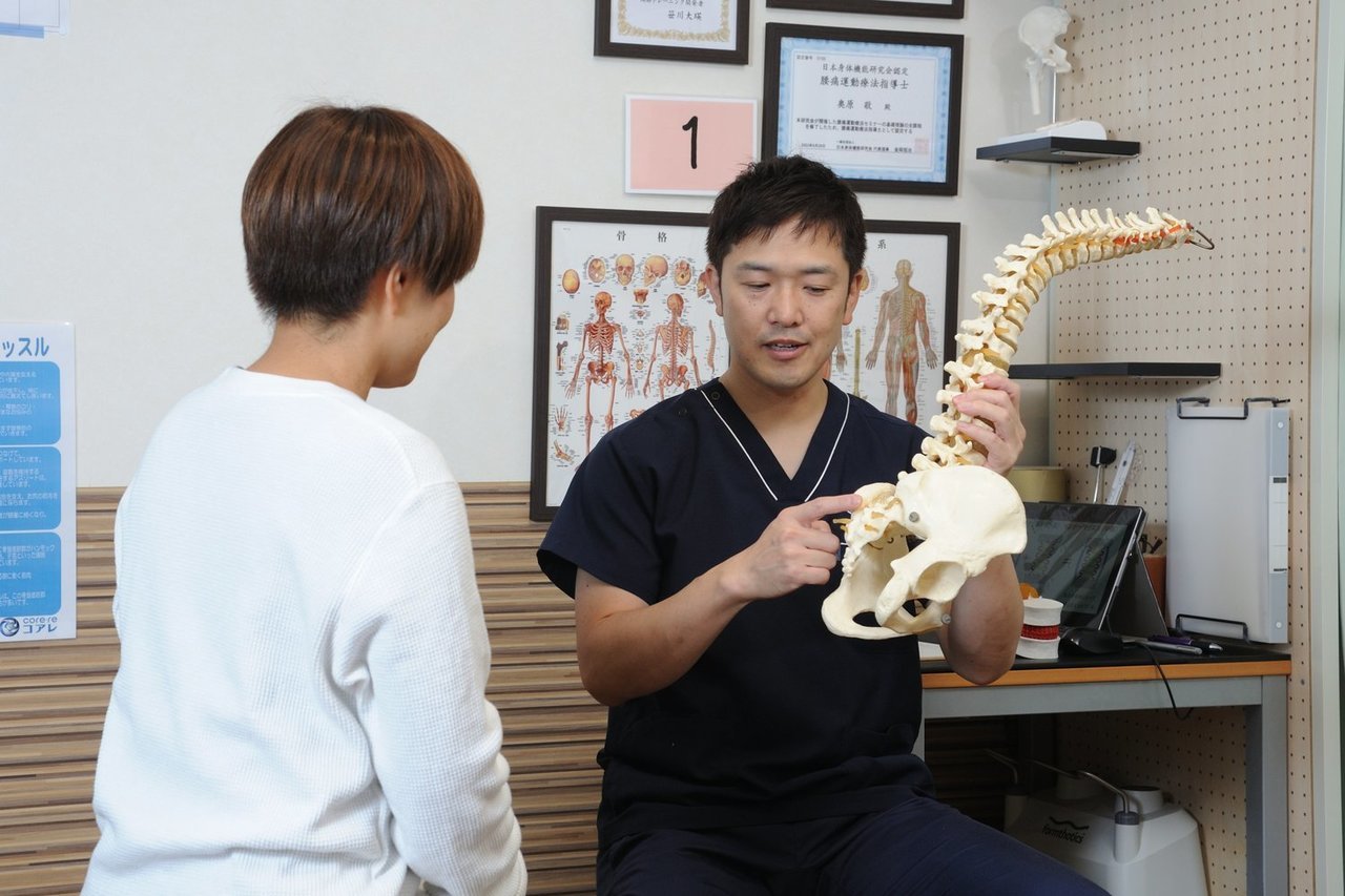 ホワイトボードや資料を用いて、脊柱管狭窄症の原因を分かりやすく説明している場面