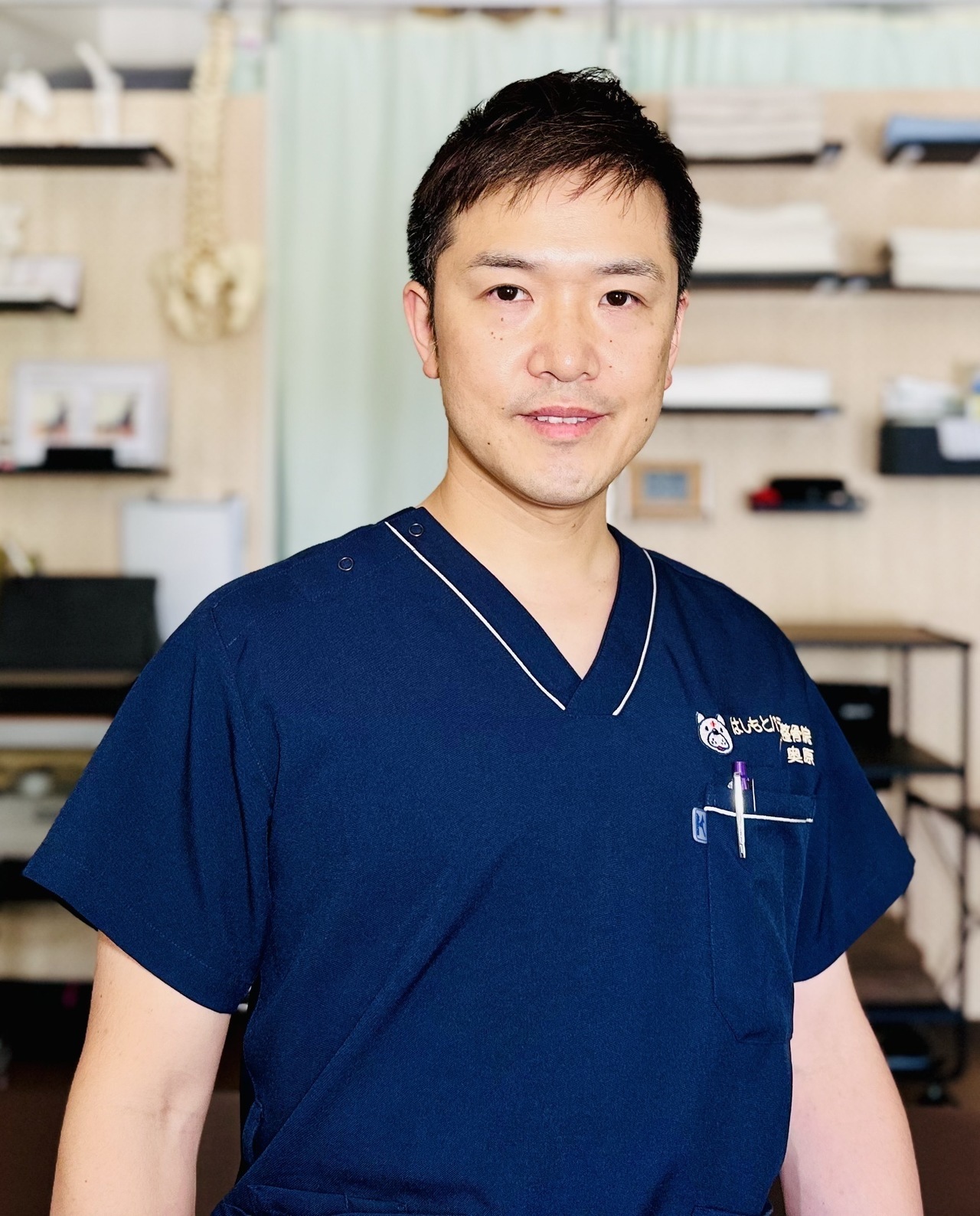 院長の奥原が正面を向いて笑顔で立っている写真。坐骨神経痛の方を安心して任せられる施術者を紹介する画像