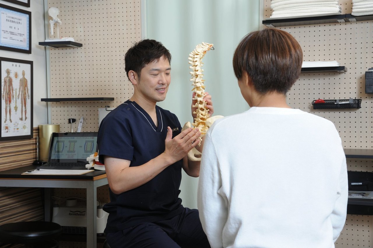 ホワイトボードや資料を用いて、坐骨神経痛の原因を分かりやすく説明している場面