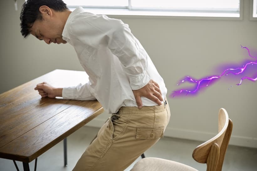 腰に強い痛みを感じて手を当てている人物の写真。坐骨神経痛による腰のしびれや痛みを表現した画像